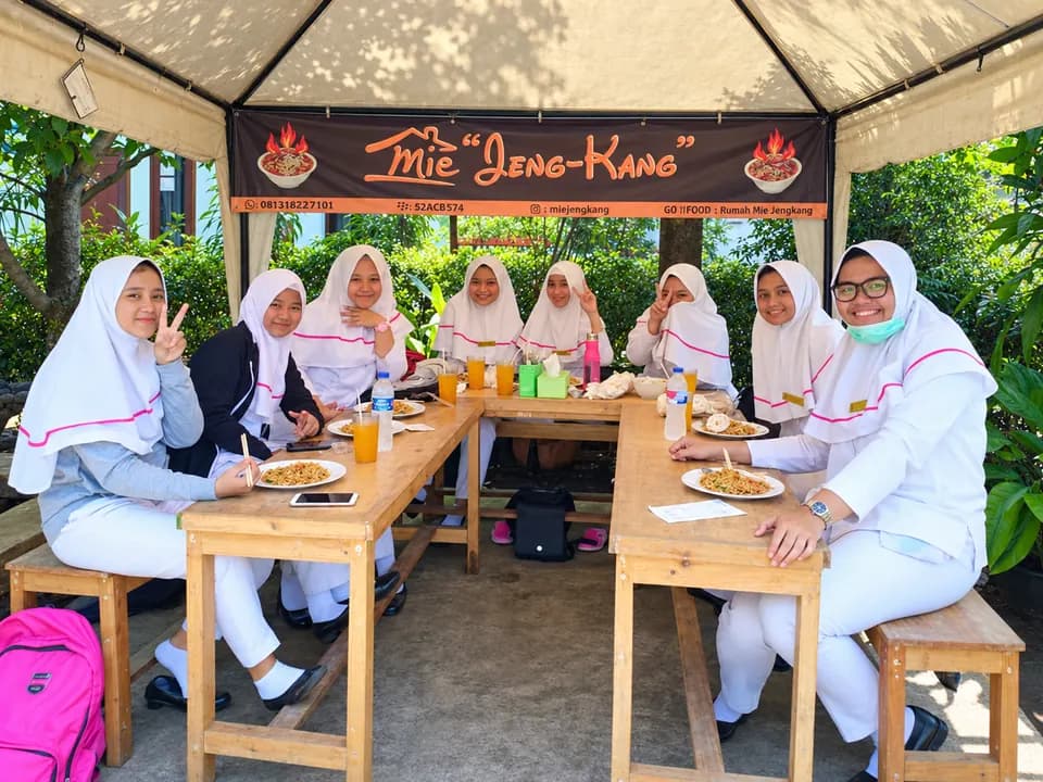 Rombongan pelajar berhijab putih makan bersama di bawah kanopi Mie Jeng-Kang